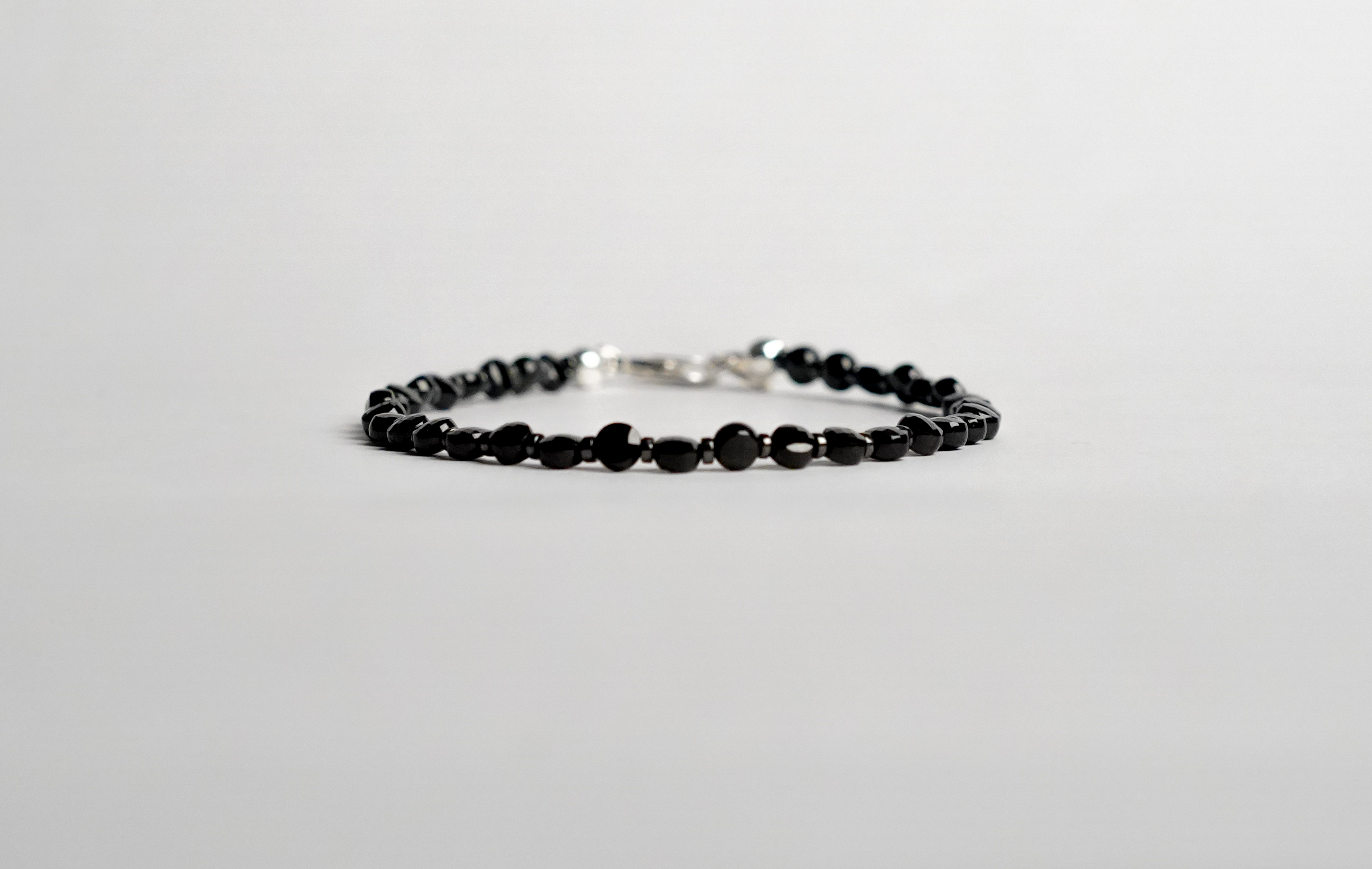 Il bracciale è realizzato con Spinello nero a forma di moneta sfaccettato ed ematite. Con pratica chiusura a moschettone in Argento sterling 925. Fatto completamente a mano in Italia.