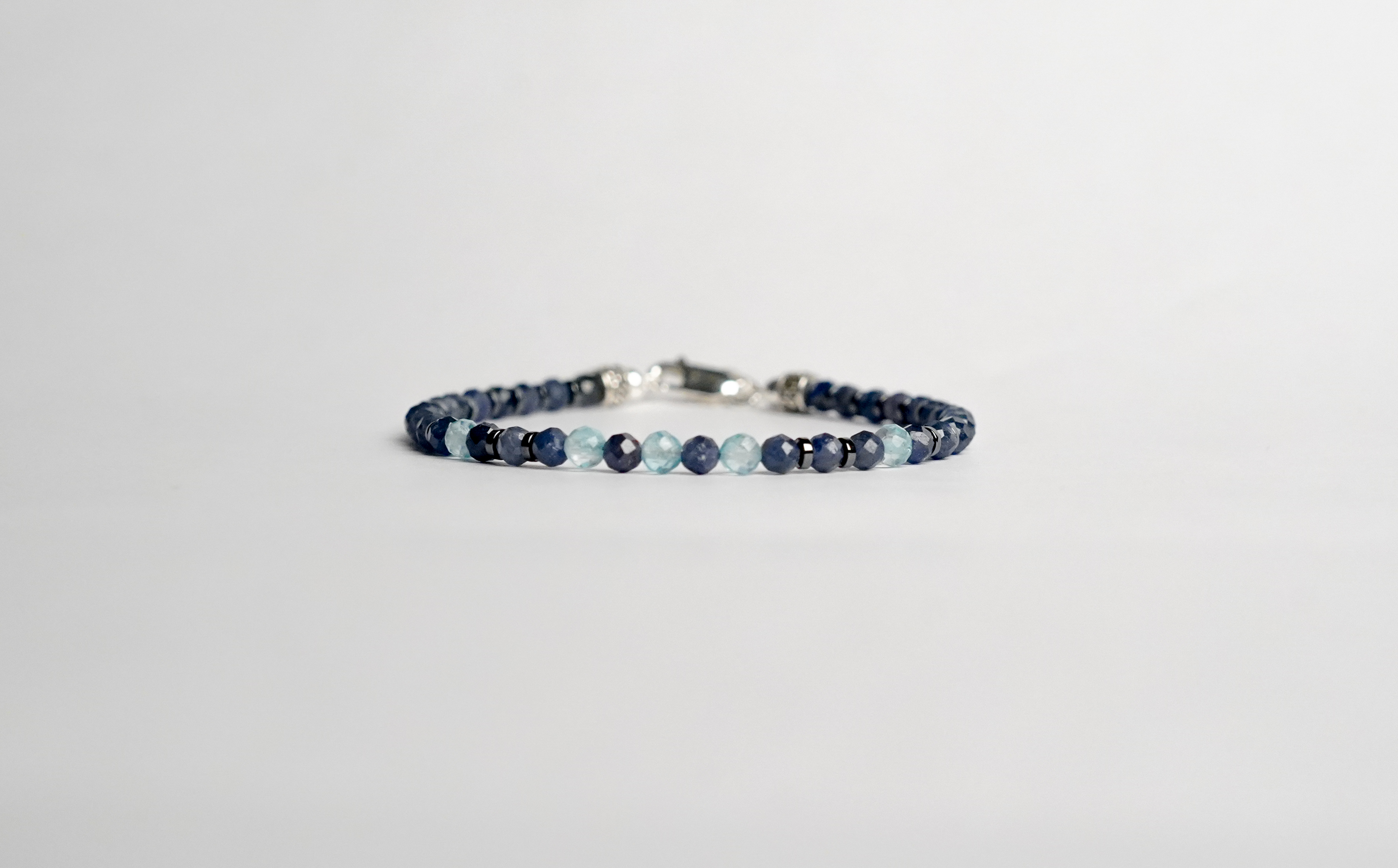 Il bracciale è realizzato con gemme di Zaffiro blu, Topazio azzurro svizzero ed ematite. Rifinito con accenti in Argento sterling 925 e pratica chiusura a moschettone in Argento sterling 925. Realizzato con le gemme più belle per un gioiello dal fascino unico e raro. Fatto completamente a mano in Italia.